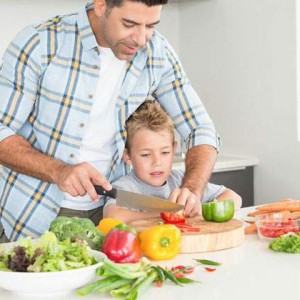 father teaching son how to cut vegetables